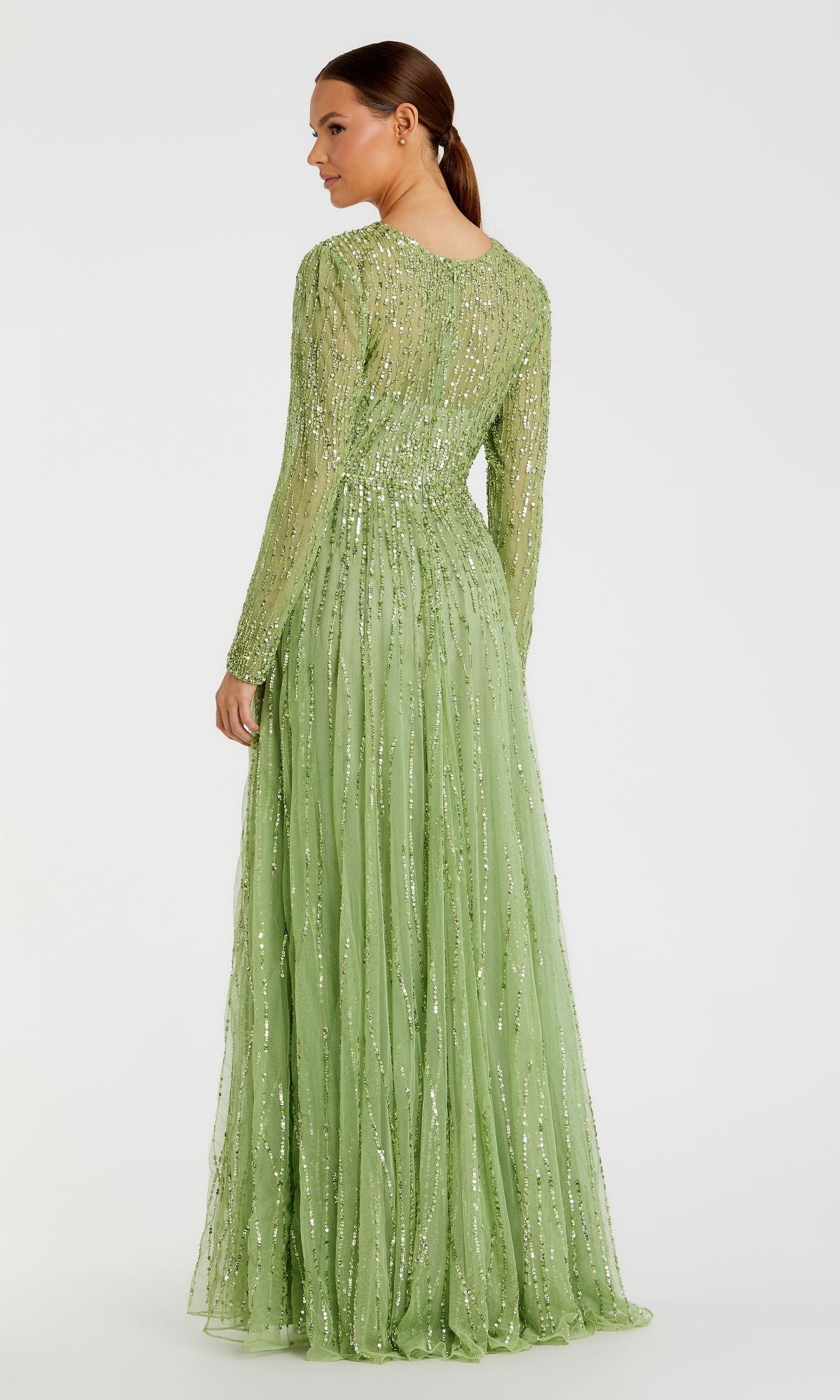 A woman faces away in the Mac Duggal 5636 modest long sleeve formal dress, highlighting its flowing skirt and elegant light green sequin design against a plain white background.